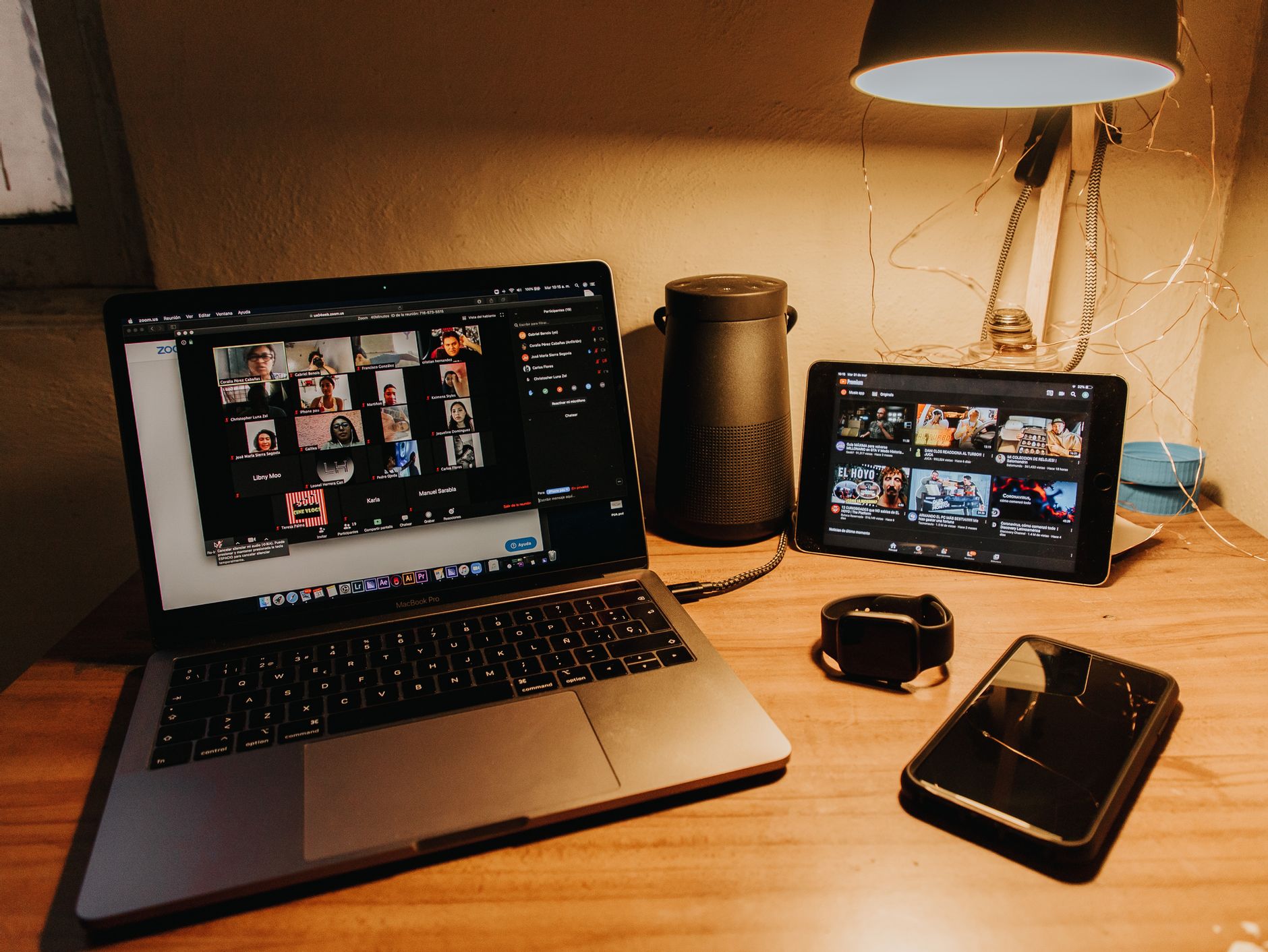 Laptop setting on a warmly lit desk displaying a zoom meeting of numerous people.